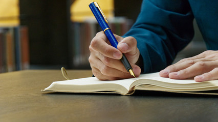 Close-up of businessman in suit writing on notebook on desk. A blue fountain pen holding in right hand. Isolation and working at home during coronavirus pandemic