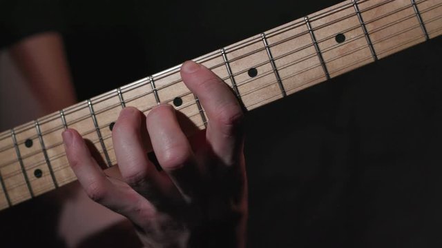 Male guitarist plays blues style riff on electric guitar, close up on hand and middle of fretboard.