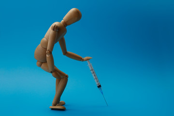 Wooden man figure is in a tired pose the man leans on the syringe as on a walking stick. Concept of fatigue from a long illness and high fever