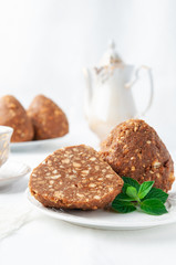 Funnel cake homemade. Cut in half. Lies on a white plate. Decorated with mint. In the background is a cup of tea with a teapot and a plate with cake. The background is white. Close-up.