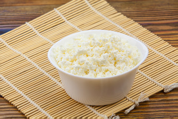 Tasty fresh grained cottage cheese on a plate on  wooden table