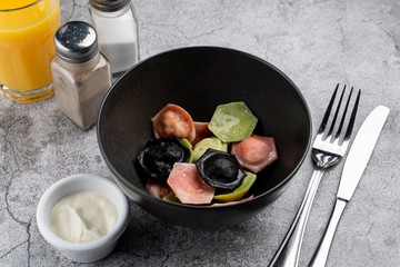 Multicolor dumplings with a bowl of sour cream as a part of kids menu