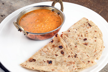 Handmade flat bread chapati and dal tadka fry in brass bowl pan on white plate rustic wooden background - obrazy, fototapety, plakaty