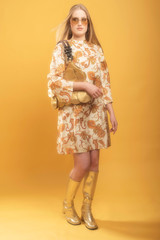 Fashionable blonde woman in vintage paisley dress and sunglasses holds handbag.