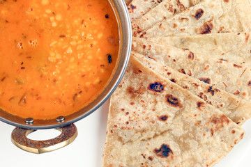Handmade flat bread chapati and dal tadka fry in brass bowl pan on white plate rustic wooden background