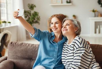 Happy mother and daughter taking selfie on couch.