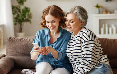 Cheerful mother and daughter using smartphone on sofa.
