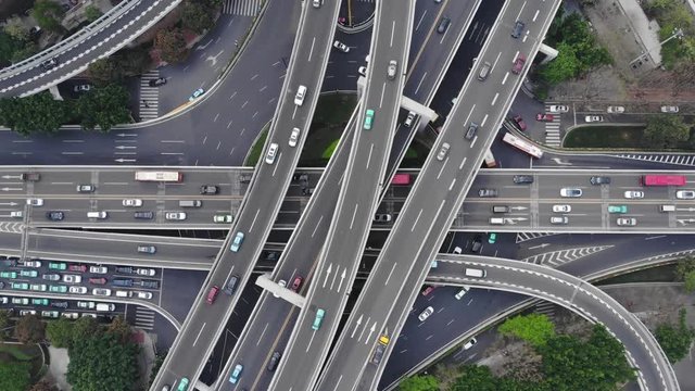 Stacked road levels at complex junction, top-down aerial shot. Large elevated roundabout and many overpasses above. Lively traffic on lanes, camera look straight down and lift up
