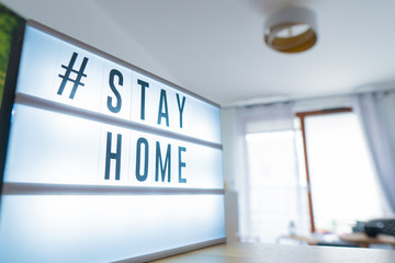 Coronavirus home sign lightbox with text hashtag #STAYHOME glowing in light. COVID-19 banner to promote self isolation staying at home. Apartment background