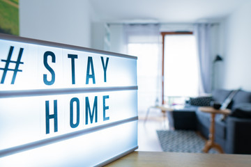 Coronavirus home sign lightbox with text hashtag #STAYHOME glowing in light. COVID-19 banner to promote self isolation staying at home. Apartment background