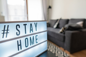 Coronavirus home sign lightbox with text hashtag #STAYHOME glowing in light. COVID-19 banner to promote self isolation staying at home. Apartment background