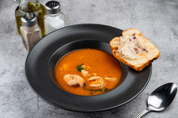 Hot and spicy tomato seafood soup with salmon, prawns and squids, close up