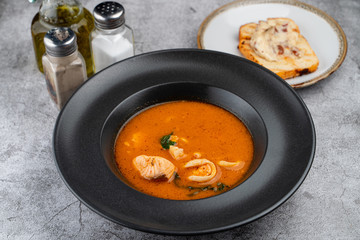 Hot and spicy tomato seafood soup with salmon, prawns and squids, close up