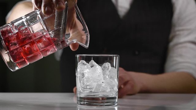 A close-up in the night bar. The bartender pours the finished cocktail into the glass. A beautiful drink supply is important in the industry.