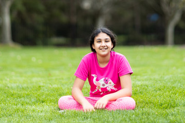 Fototapeta premium Outdoor Portrait of a Smiling Young Girl Sitting on Grass