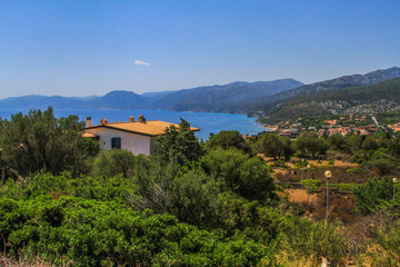 Fototapeta na wymiar House on a hill over the sea and village at the coast of the Mediterranean Sea