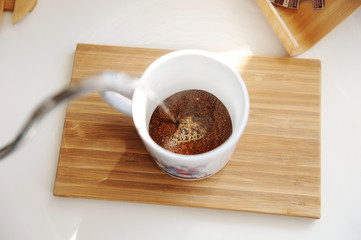 Brewing coffee in mug. Pouring water from gooseneck kettle into cup with freshly ground coffee top view