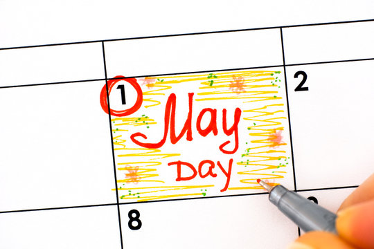 Woman fingers with pen writing reminder May Day in calendar.