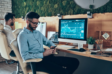 Good looking young man in shirt and eyewear using smart phone wh