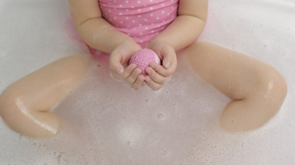 Hands of girl puts bath bomb to water. Ball of bath salt dissolves in water