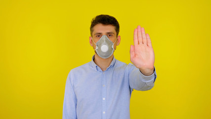 Stop virus concept: coronavirus, flu. Man in protective medical mask looks at the camera. The guy in the blue shirt shows stop on a yellow background