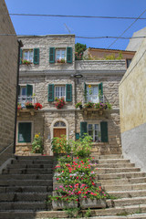 Mediterranean architecture: Narrow staircase and facade of bricked house with wooden shutters and flowers in Sardinia, Italy