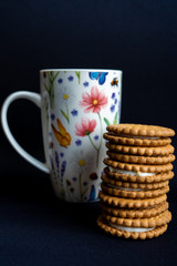 A pile of cookies and a coffee cup on dark black background, side view