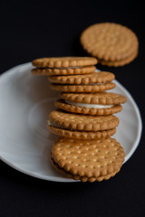 bunch of cookies are arranged on white plate on dark black background, top view