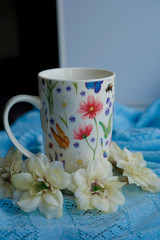 Composition made of cup with floral pattern and headband of artificial flowers on light blue textile, side view