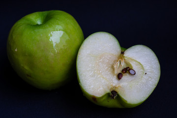 One whole green sour apple and one half of the apple on dark black background