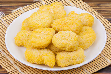 golden chicken nuggets on a white plate on  wooden background