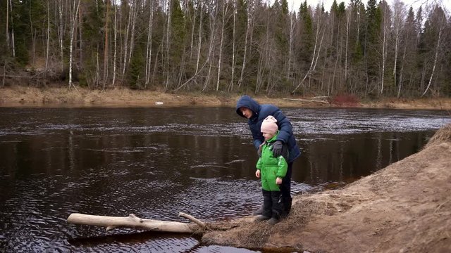 dad and daughter on the Bank of the river are standing and talking.In the fall or spring.They are dressed in jackets, dad points distance, this is family, baby in green clothes, listens to her father
