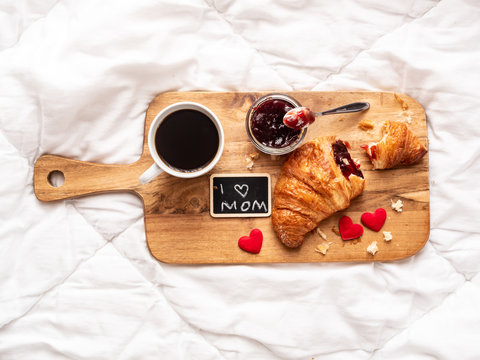 Muttertag Brunch im Bett mit frischen Croissant, eine Tasse Kaffee und Erdbeermarmelade auf einem Serviertablett, wei&szlig;e Bettw&auml;sche, Draufsicht