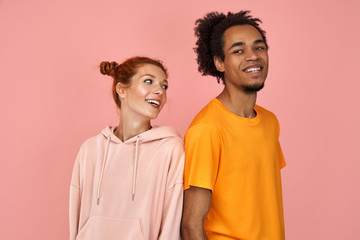 Fototapeta premium Delighted handsome black male and ginger female rejoice successfully passed exam, look happily at each other, laugh at good joke, express positive emotions, isolated over pink background
