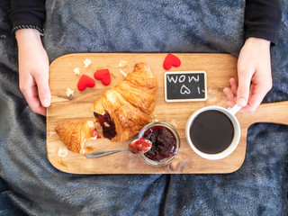 Frau mit einem Serbiertablett mit frischen Croissant, eine Tasse Kaffee und Erdbeerkonfitüre auf...