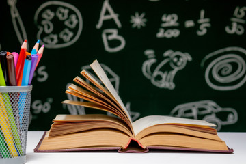 Back to school background with books, pencils and globe on white table on a green blackboard background.