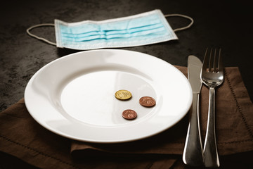 Euro cents coins on white empty plate and medical mask on black background. Lack of money during quarantine, poverty and unemployment concept.