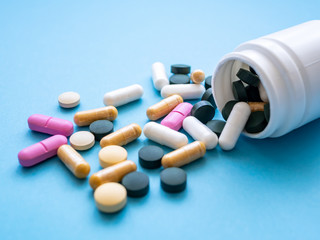 Bunte Tabletten und eine weiße Pillendose auf einem blauen Hintergrund, Nahaufnahme, Medikamente