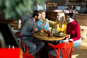 People have dinner together at a table in a cafe. Happy friends eat burgers and drink cocktails in the restaurant