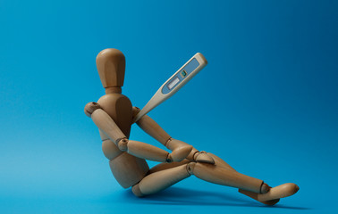 Wooden man figure is sitting with a degree meter/thermometer . Concept of fatigue from a long illness and high fever. 39 degrees Celsius on a clinical electronic thermometer.