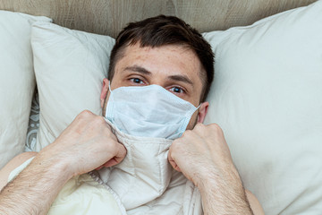 Frightened man in a medical mask lies in bed