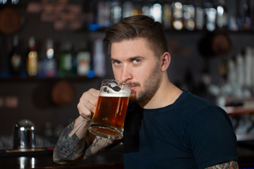 Young man sitting at bar counter with a pint of light beer