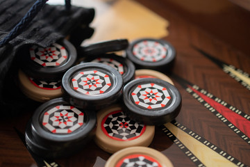 Obraz na płótnie Canvas Black and white patterned backgammon chips fell out of the black bag and scattered on the open game Board