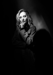 Beautiful girl wearing a casual trendy trousers, turtleneck glasses and raincoat posing on a dark background in the shadows. Fashionable, advertising, lifestyle and commercial monochrome design.