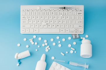 Shopping cart toy with medicaments and Keyboard. Pills, blister packs, medical bottles, thermometer, protective mask on a blue background. . Health care and internet shopping