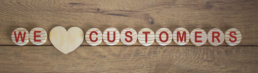 Wooden small circles with words we love customers on wood background. Concept image.