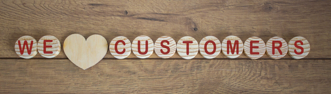 Wooden small circles with words we love customers on wood background. Concept image.
