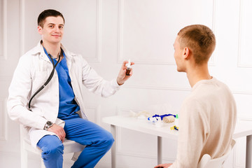Obraz premium Male handsome doctor shoving a nose drops to young male boy patient. Protection from virus covid19, coronavurus. Concept of healhtcare.