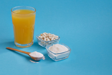 Collagen protein powder and capsules in jar, a glass of orange juice on blue  background. Natural beauty and health supplement for skin, bones, joints.