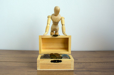 Wooden model of a man behind the small wooden coin chest.